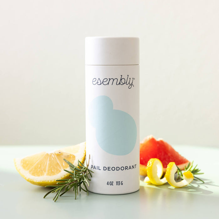 Esembly's Pail Deodorant that's in a white cardboard shaker with a light blue splotch next to citrus fruit and rosemary