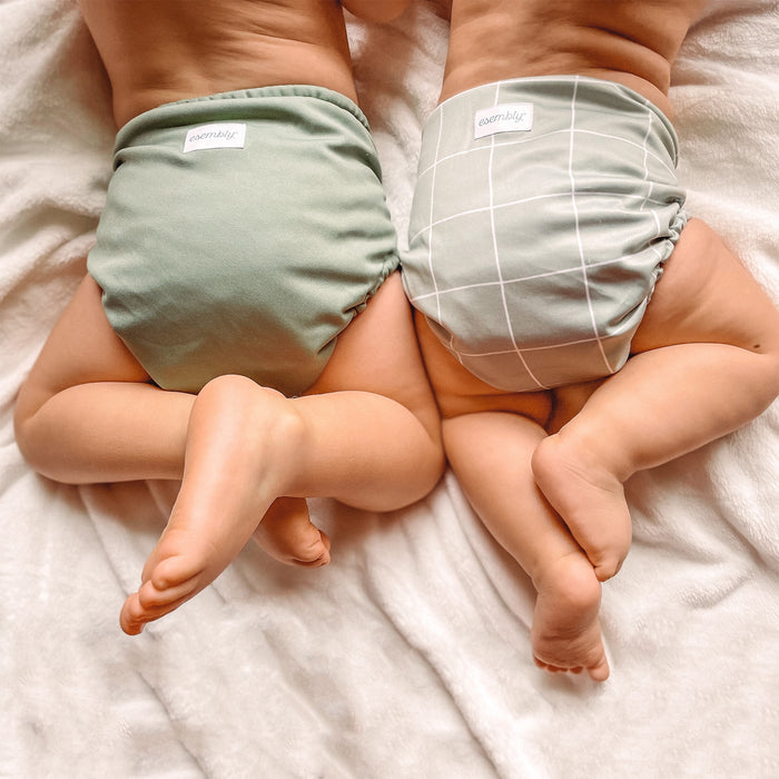 One baby wearing a mid-green tone Outer and one baby wearing a light mint green with white grid lines Outer