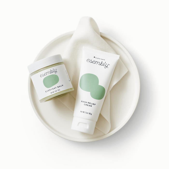 Esembly Rash Relief and Everyday Balm laying on top of a white piece of fabric and white plate