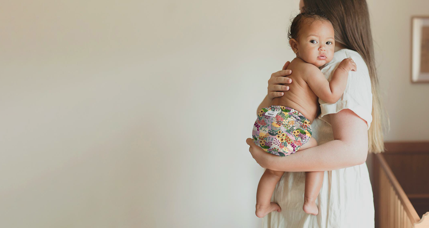 Mom holding baby wearing an Esembly Outer in Botanic Garden (a hand painted floral print)