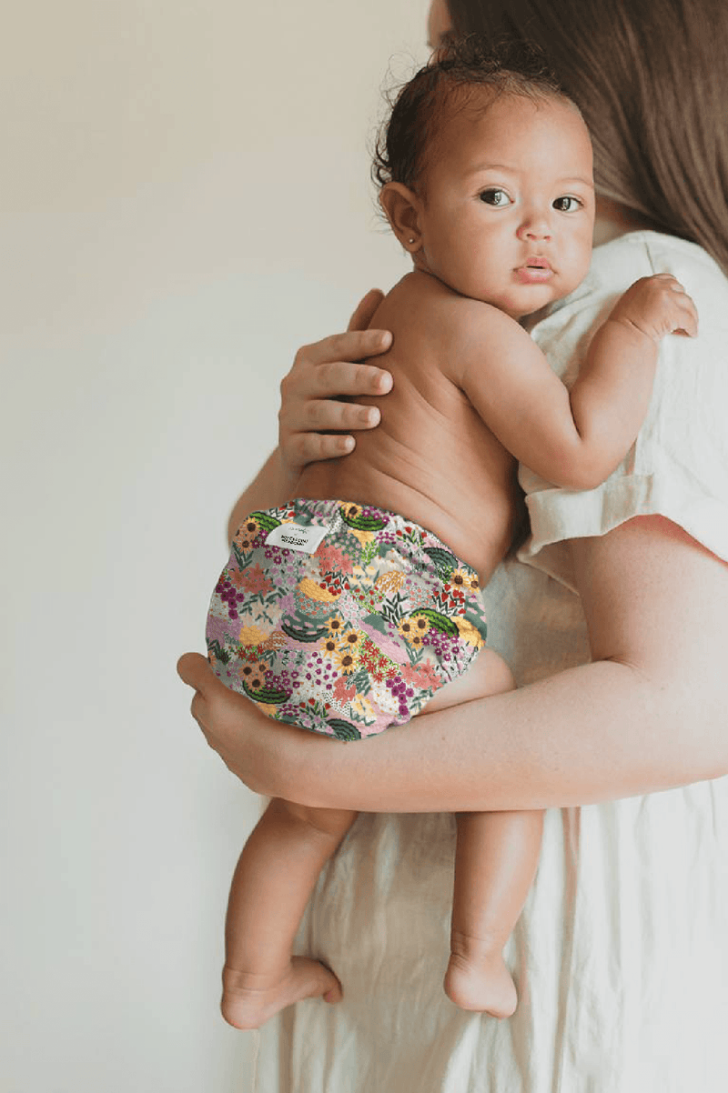 Mom holding baby wearing an Esembly Outer in Botanic Garden (a hand painted floral print)