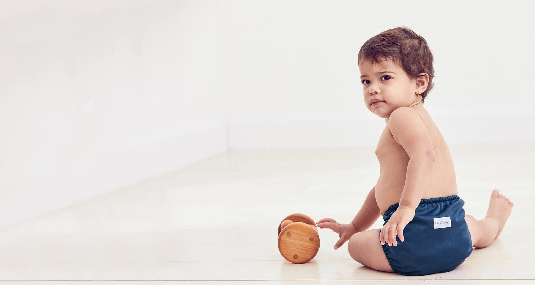 A baby playing with toys on the floor and wearing an Esembly diaper in dark navy