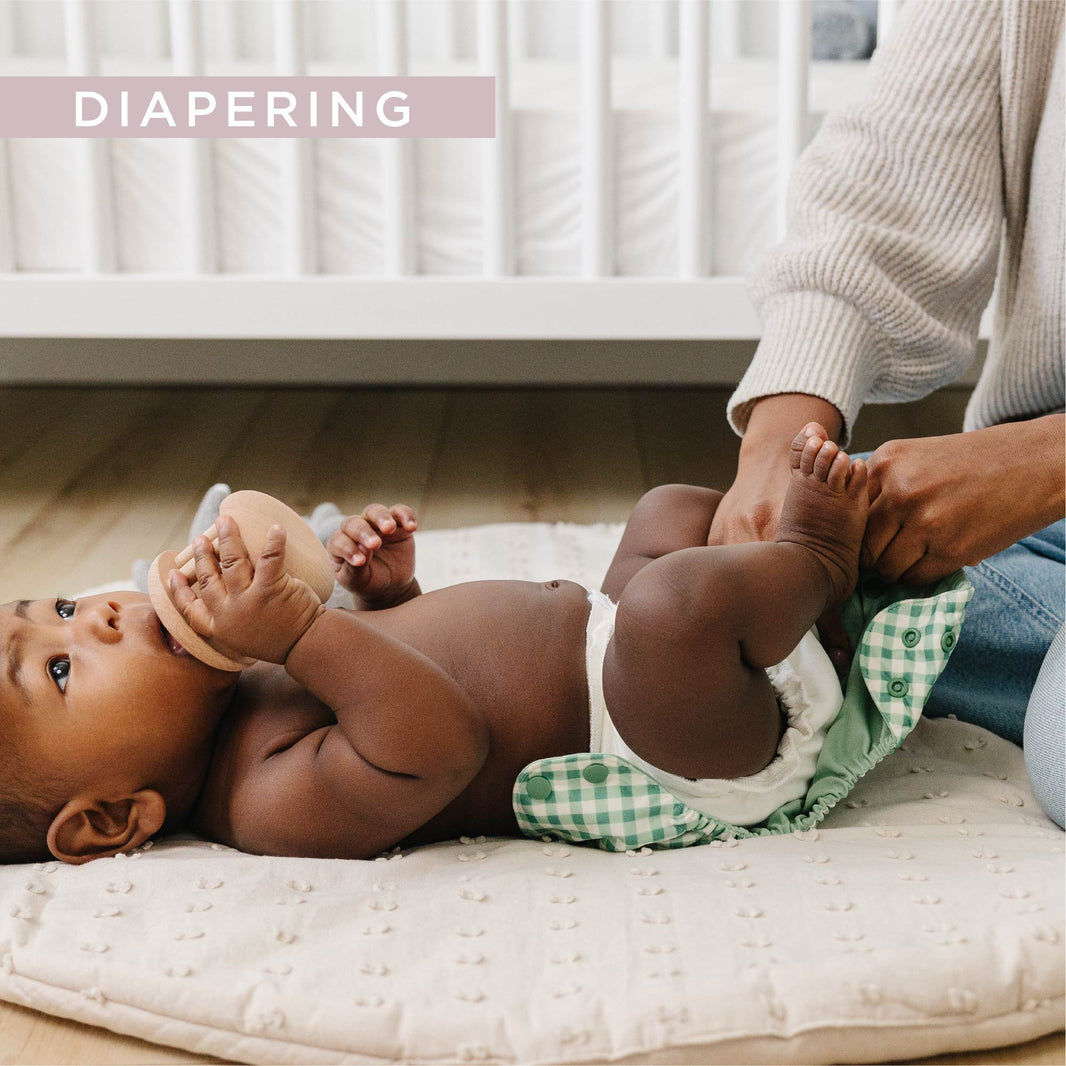 Baby on back getting cloth diaper change with green cover