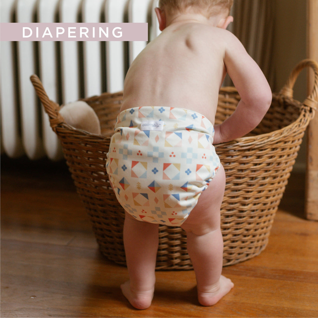 Baby in cloth diaper reaching  into laundry basket