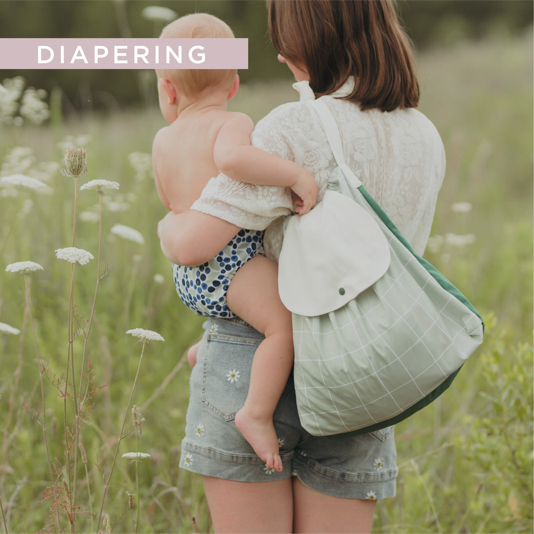 Mom holding baby in cloth diaper and carrying a wet bag