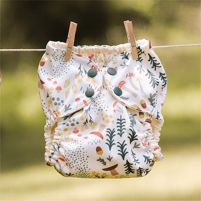 A Fantastic Fungi Outer (an off-white background with colorful mushroom, trees, and leaves illustrations) hanging on a laundry line with clothing pins