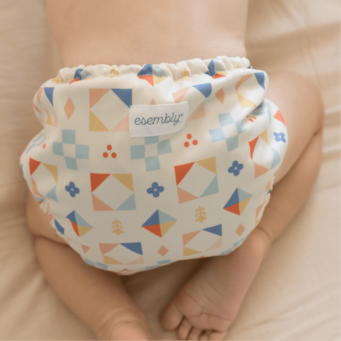 Baby wearing a colorful geometric patterned diaper with 'esembly' label.