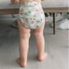 Baby standing wearing a Santas Outer (a mint green Outer with illustrated Santa heads, mistletoe, and candy canes)