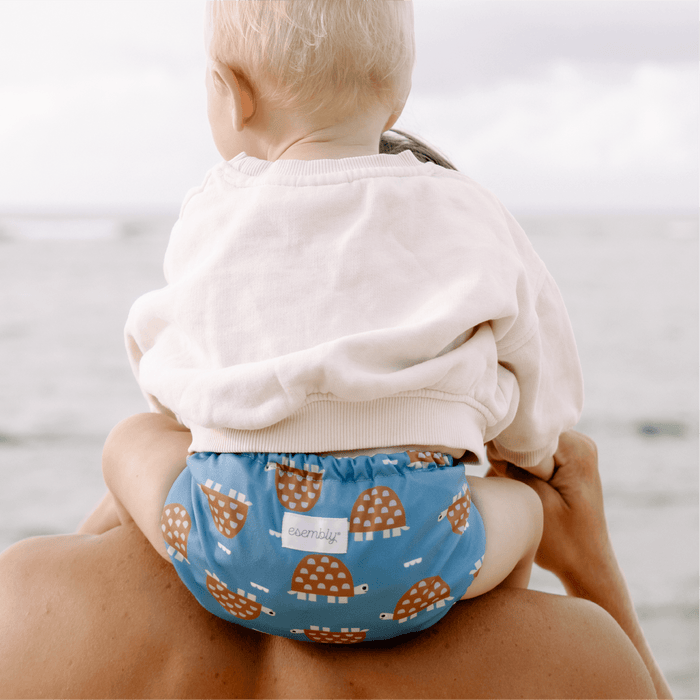 Child wearing a blue diaper with turtle pattern on a beach