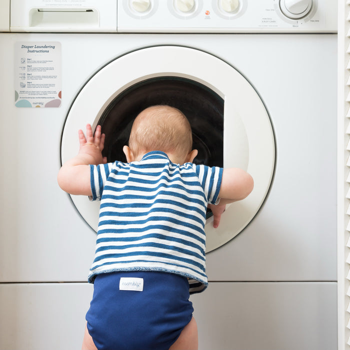 Baby wearing an Esembly Outer looking into a washer that has an Esembly Magnet on it