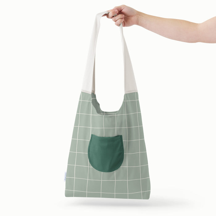A hand holding an Esembly Carryall Bag in the Lattice colorway (Lattice body, dark green pocket, and off-white strap)