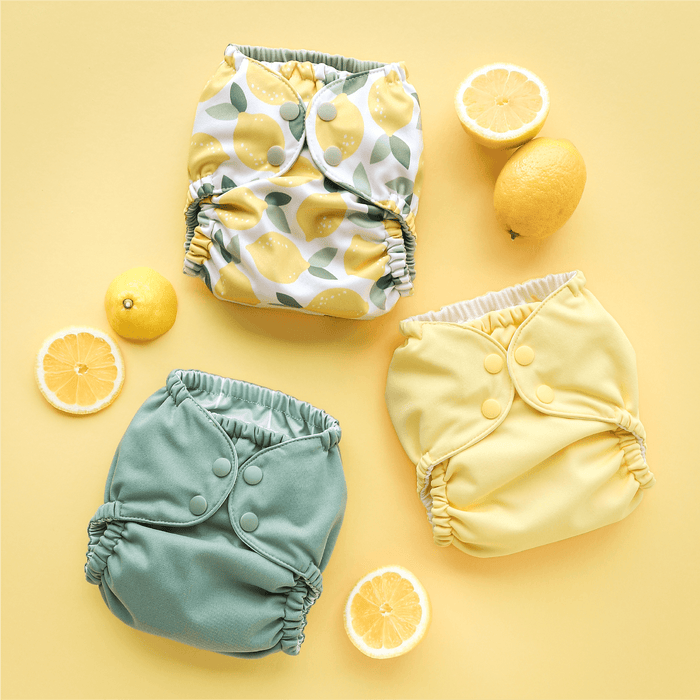 Three colorful baby diapers on a yellow background next to lemons