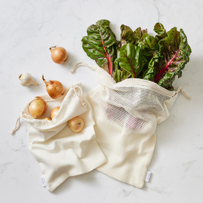 Onions and rainbow chard coming out the top of Esembly's Produce Savers that are sitting on a marble countertop