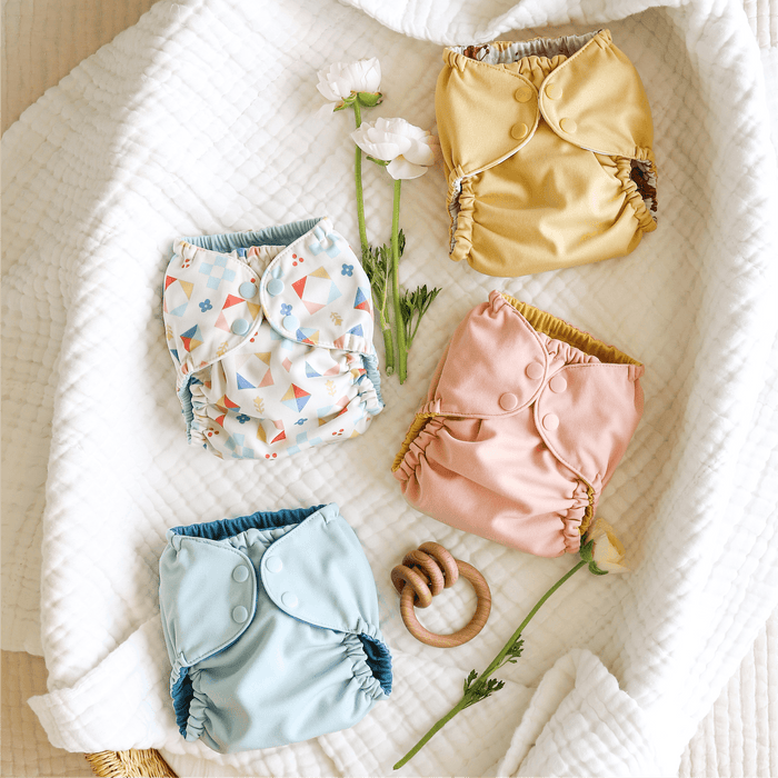 Colorful baby diapers and a wooden ring on a white textured surface with flowers.