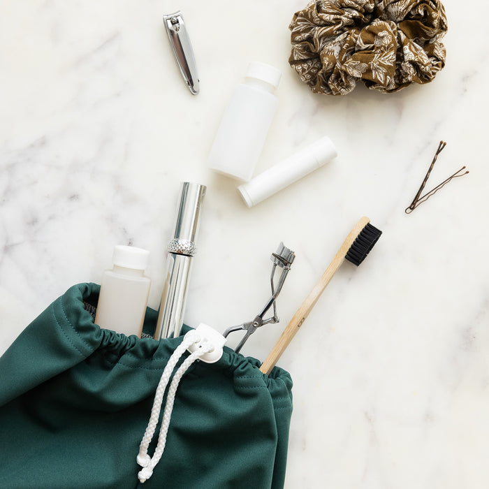 Front view of a dark green waterproof bag with toggle close top with fingernail clippers, toothbrush and cosmetics