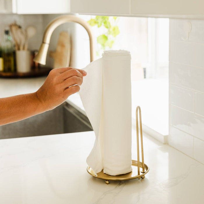 Paperless Towels on a gold paper towel stand in a kitchen with a hand grabbing a towel