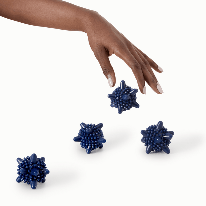 4 navy blue silicone laundry agitators with spikes with varying heights being dropped by a single hand