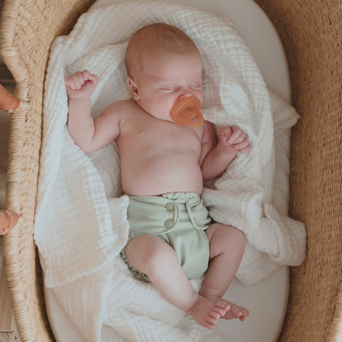 Newborn baby in a crib with a pacifier, wearing a green Esembly diaper.