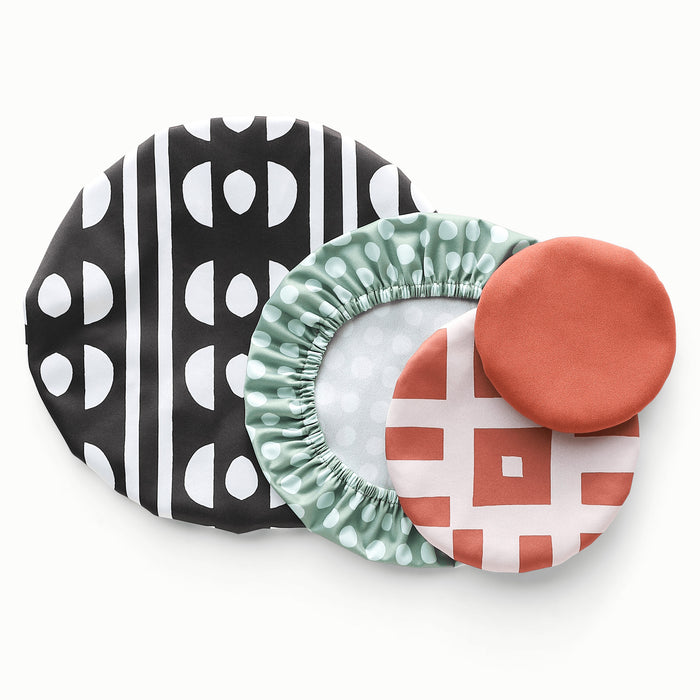 Image of four bowl caps in varying shapes. One in Circuit (a black and white pattern with a half circle and organic circle pattern), one in Stellar (a mid-tone green background with light blue organic shaped dots), one in Theory (a reddish brown square and line geometric pattern on a light purple background), and one a solid reddish brown color.