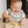 Baby wearing a Tractors Bib eating applesauce in a high chair