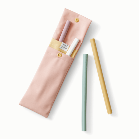 A blush straw pouch with muted yellow accents holding light purple, white, light green, and muted yellow silicone straws