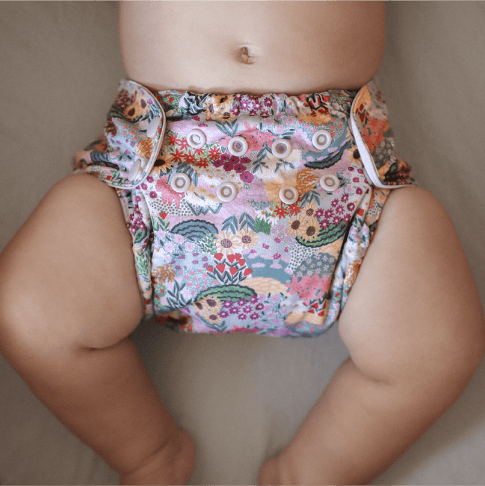 Baby laying on their back wearing an Esembly Outer in Botanic Garden (colorful florals hand painted by illustrator Sara Boccaccini Meadows)