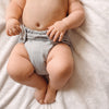 Baby laying on a white blanket wearing an Outer in a light gray color