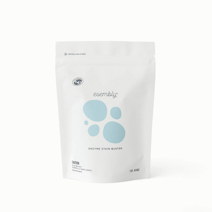 A white stand-up pouch of Esembly Enzyme Stain Buster, featuring light blue circular graphics and black text, photographed on a clean white background.