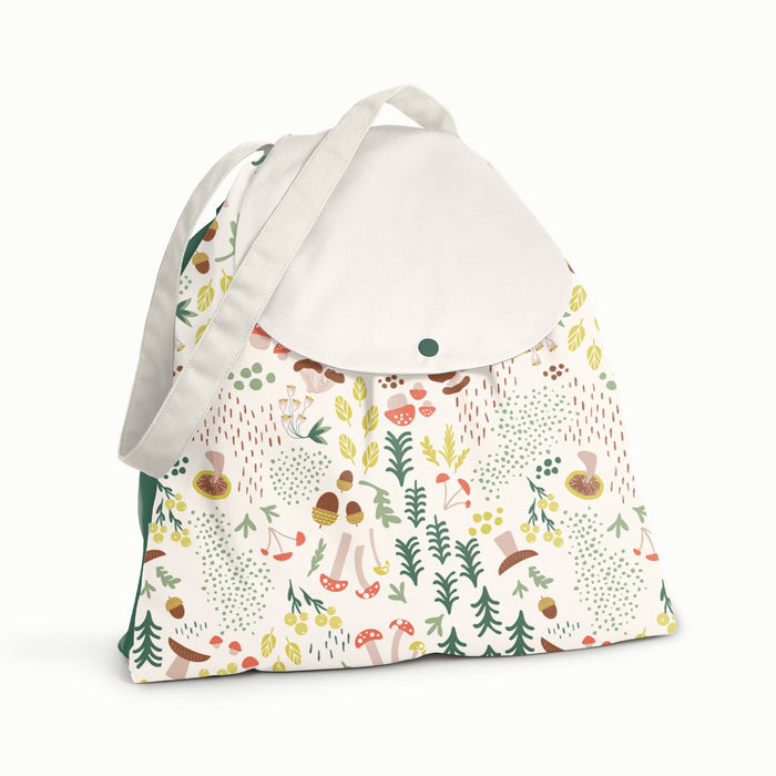 Front view of Esembly Day Bag in Fantastic Fungi with a front body with the Fantastic Fungi Pattern (an off-white background with colorful mushroom, trees, and leaves illustrations), a dark green back, and a white flap and strap