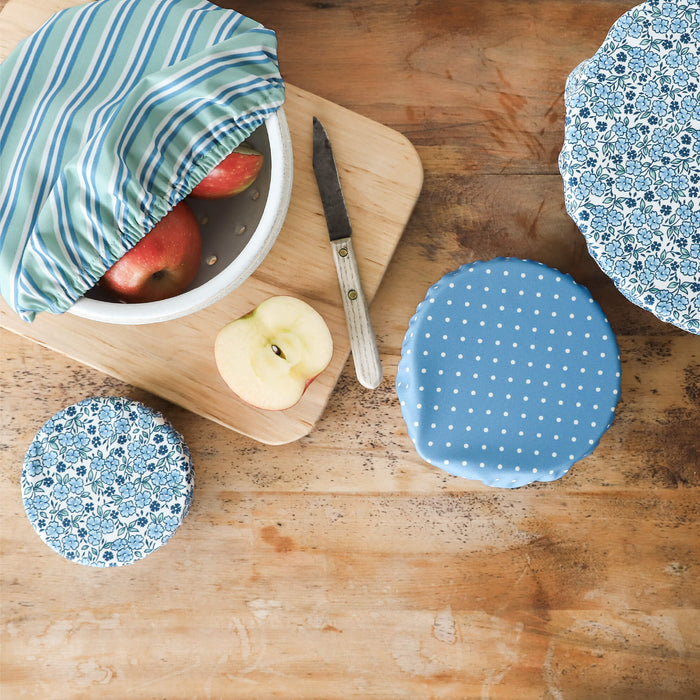 Reusable fabric food wraps on a wooden surface with apples and a knife.