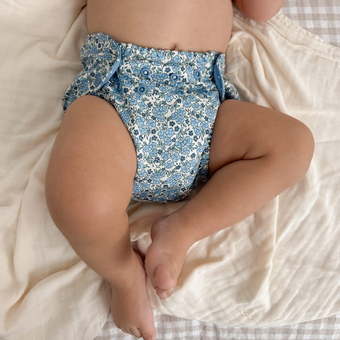 Baby wearing a blue floral diaper on a white blanket