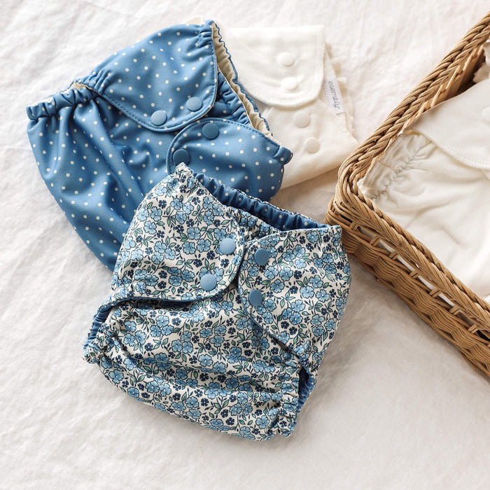 A floral Outer, white polka dots with a blue background Outer, and Inner laying on top of each other next to a basket filled with Inners.