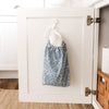 Floral-patterned bag with paperless towels coming out the top hanging on a hook inside a white cabinet.