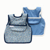 Two blue baby bibs with white trim, displayed on a clean white background. The bib in the foreground features a dense blue, white, and navy floral pattern, while the bib in the background is a lighter blue with white polka dots.