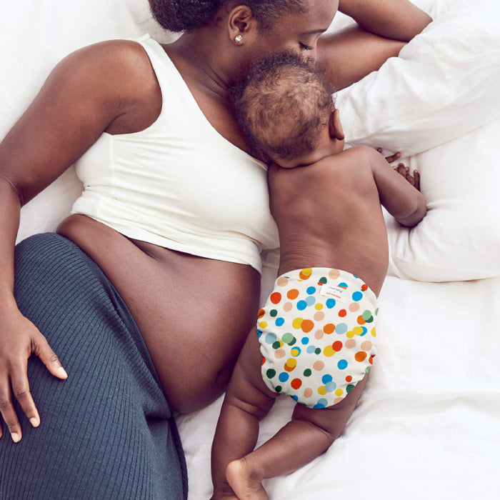 Baby and mom on a bed with the baby wearing an Esembly Outer in Funfetti