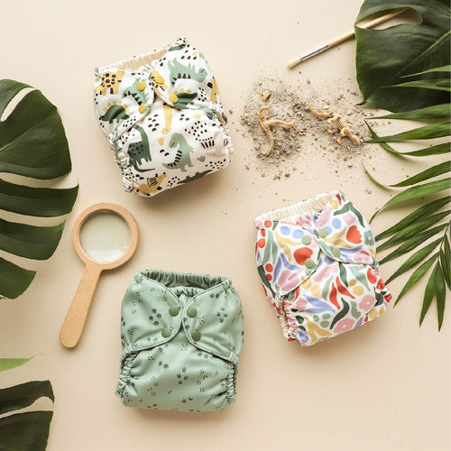 Esembly Dinosaur Collection Outers next to greenery, a wooden magnifying glass, and fossil toys and sand