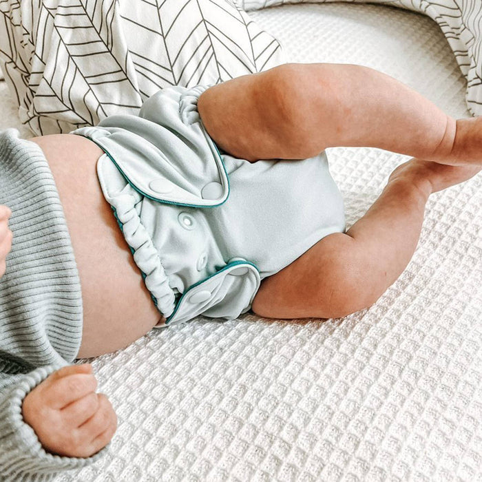 Baby laying on a white textured blanket wearing a gray sweater and a light blue Outer