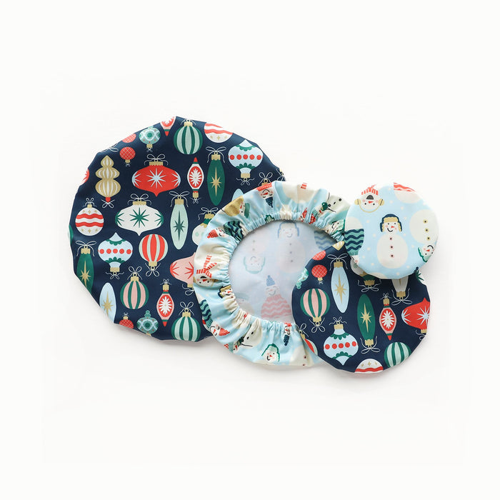 Bowl Caps in Ornaments (a dark blue outer with illustrations of colorful, vintage ornaments) and Snow Friends (a light blue background with illustrated snowmen wearing winter clothings)