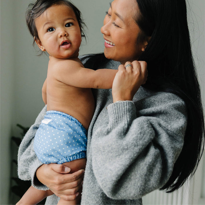 Woman holding a baby wearing a blue diaper with white polka dots.