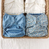 Two blue patterned cloth diapers in a woven basket with stacks of Inners