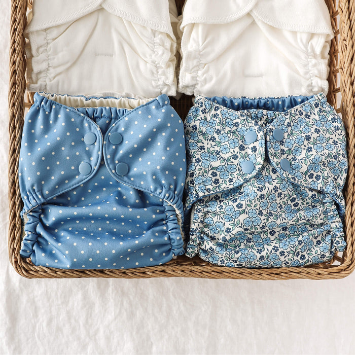 Two blue patterned cloth diapers in a woven basket with stacks of Inners