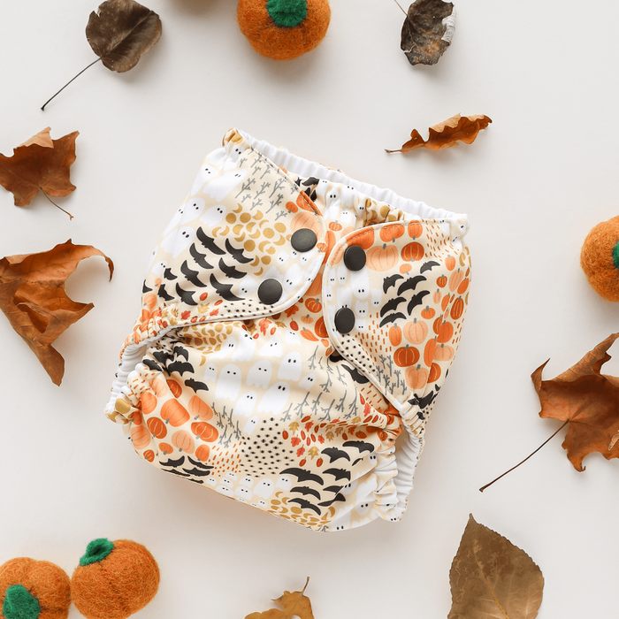 Patterned diaper with Halloween design surrounded by autumn leaves and pumpkins on a light background