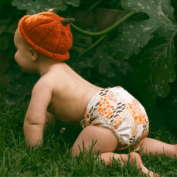 Baby wearing a knitted pumpkin hat and patterned diaper crawling on grass