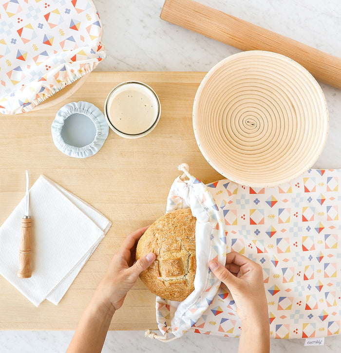 Person taking bread out of a reusable bread storage bag on a kitchen counter with various kitchen items.