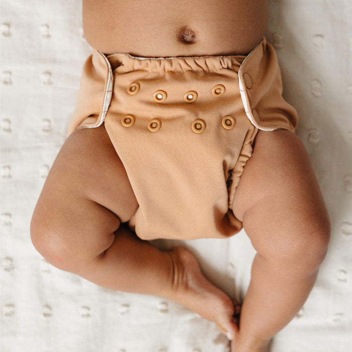 Baby wearing a light brown Outer laying on a white blanket