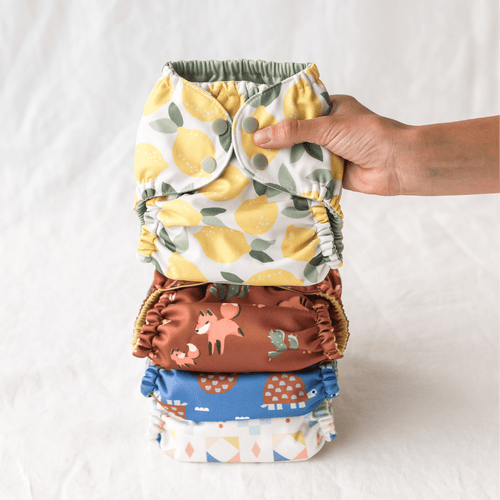 Stack of colorful baby diapers with a hand holding the top one against a white background