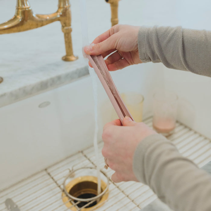 A woman opening a pink silicone straw to clean in a sink