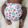 Baby laying on a white blanket wearing an Outer with a white background with red strawberries and light green leaves