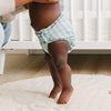 Child wearing a striped diaper standing on a white rug.