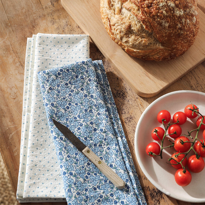 Tea Towels with floral pattern and polka dots on a wooden surface with bread and tomatoes